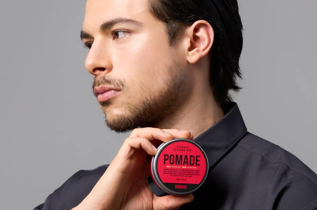 A man with a combed side part holding a red tin of DASHU Red Pomade