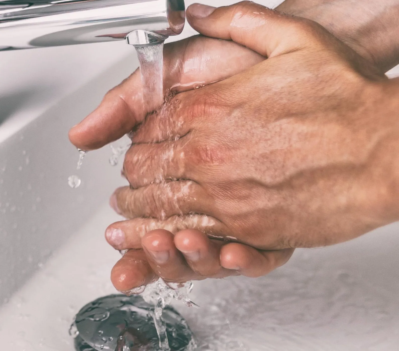 Hands rinsing pomade off under a running tap