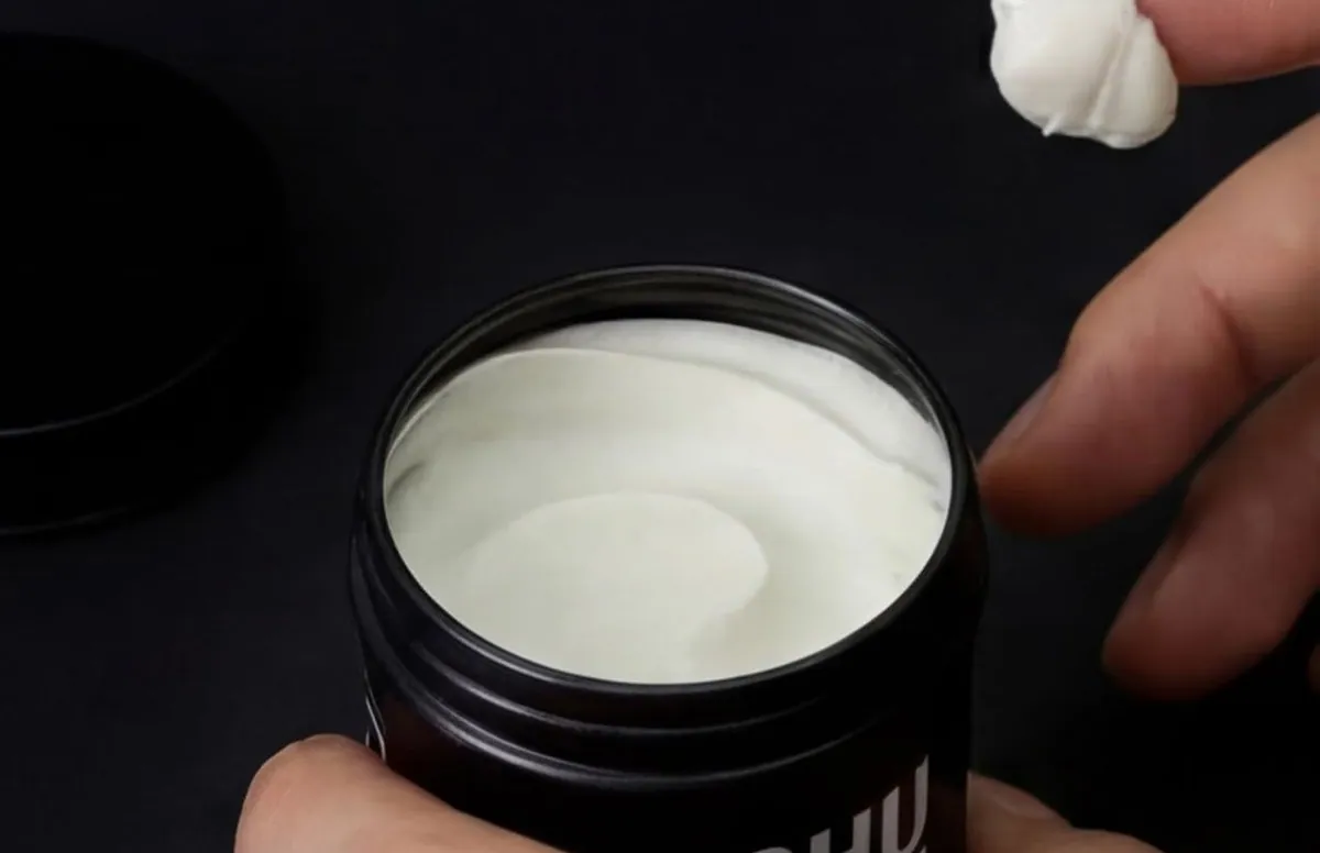 An open black jar of DASHU Original Super Mat Hair Wax with a fingertip of wax beside it