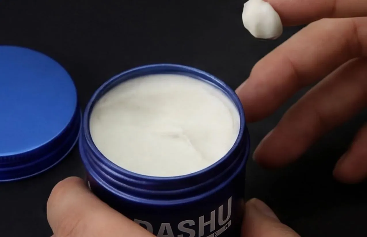 A fingertip of wax lifted from an open blue jar of DASHU Ultra Holding Power Wax