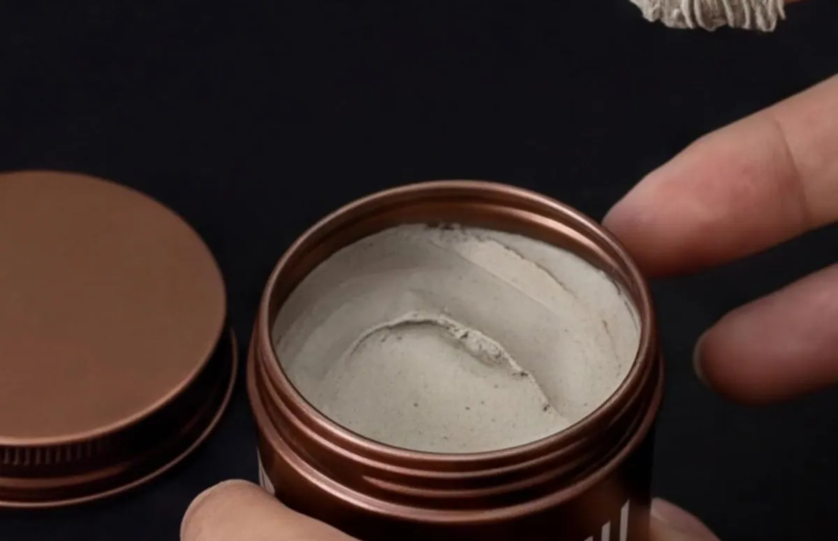 An open brown jar of DASHU Wild Design Muscle Wax showing its clay texture